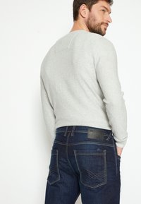 Grijs gestreepte langemouwen shirt gecombineerd met donkerblauwe spijkerbroek met decoratieve stiksels, een leren label en een klassiek zakontwerp.