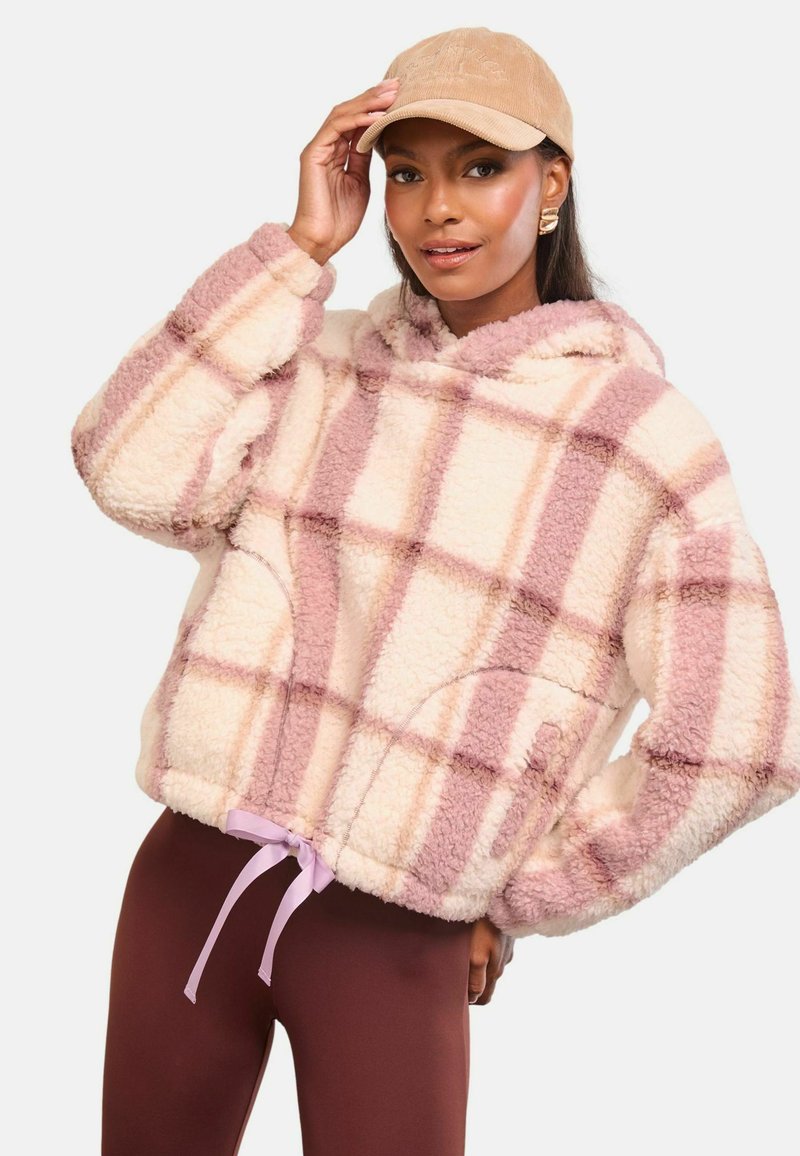 Vattás, kockás mintázatú kapucnis pulóver krém és világos rózsaszín színben, zsinóros aljjal. Magas derékú, barna leggings-szel párosítva.