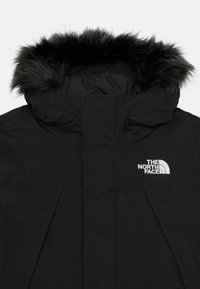 Parka noire avec capuche en fausse fourrure, fermeture éclair à l'avant et logo sur la poitrine gauche. Le tissu semble texturé et résistant.