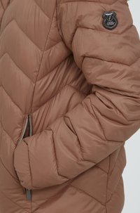 Smeđi puffer jakna s chevron uzorkom, sa zatvorenim džepovima i kružnom oznakom na rukavu. Glatki, sjajni materijal.