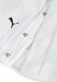 Cămașă albă cu capse metalice și un logo Puma negru. Are o textură netedă și un design clasic al gulerului.