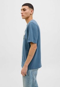 Blaues T-Shirt mit kurzen Ärmeln aus weichem Baumwollmix, mit einem Grafikdruck auf der Vorderseite und einem lässigen Schnitt. Helle blaue Denim-Hosen.