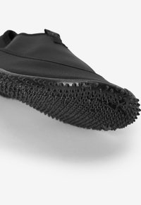 Schwarzer Slipper mit einem glatten Obermaterial, ausgestattet mit einer strukturierten Gummisohle, die mit kleinen saugnapfartigen Griffen für Halt versehen ist.
