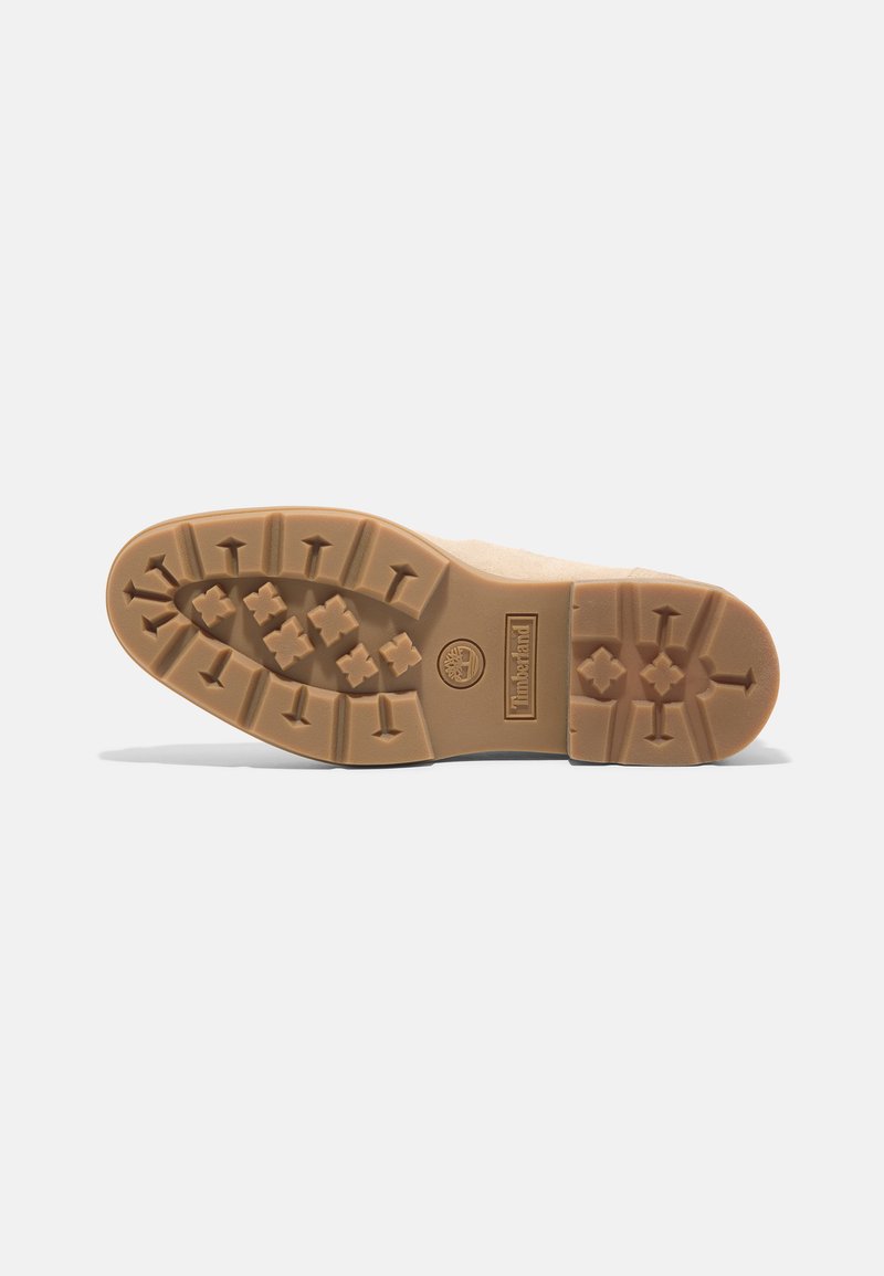 Semelle en caoutchouc beige avec un motif de traction rugueux, comportant des formes hexagonales et en flèche pour une meilleure adhérence. Logo Timberland présent sur le côté.