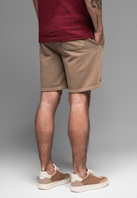 Beige bavlněné šortky s volným střihem, které mají boční kapsy a malou značkovou detail. V kombinaci s krémovými a béžovými teniskami.