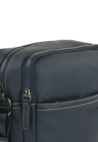 Bolso de cuero azul marino con doble cremallera, costuras en contraste y un acabado texturizado. Presenta un bolsillo frontal y una correa ajustable.