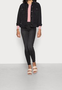 Chaqueta de mezclilla negra sobre una blusa rosa, combinada con jeans skinny negros y tacones nude con tiras. Texturas suaves, siluetas ajustadas y colores contrastantes.
