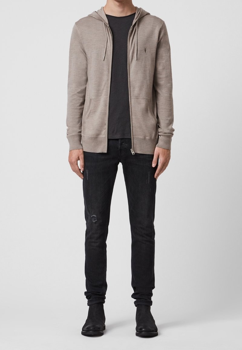 Sweat à zip beige clair avec capuche à cordon, porté sur un t-shirt noir, associé à un jean noir et des bottines noires.