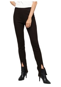 Bruna figursydda byxor med sidoklipp i fållen, tillverkade av ett slätt tyg. Matchas med svarta högklackade ankelstövlar.