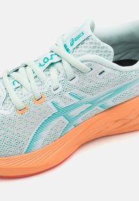 Baskets de course bleu clair avec une tige en mesh, accents teal et semelle orange. Comprend des détails texturés et des motifs rayés sur le côté.