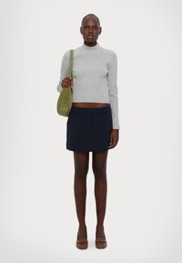 Maglione grigio a coste con colletto alto, gonna mini plissettata blu navy, borsa a tracolla in suede verde e scarpe con tacco marroni. Stile pulito e minimalista.