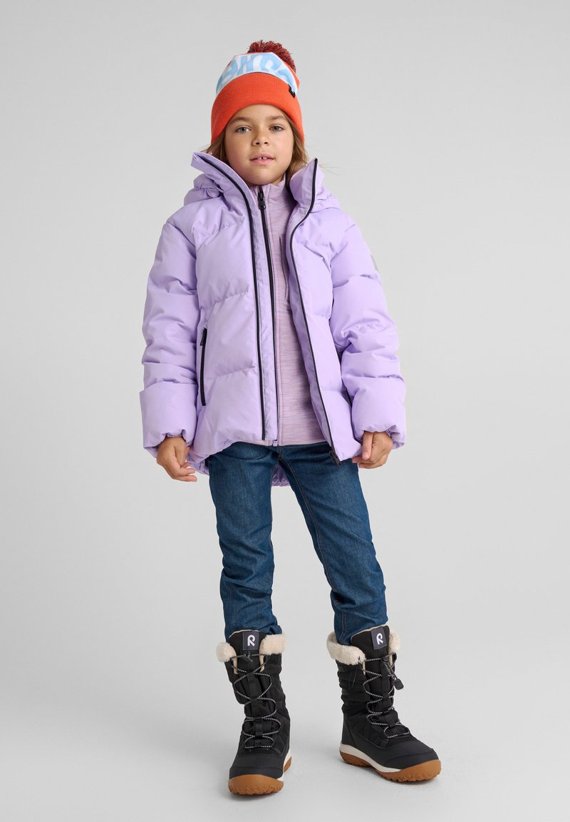 Giacca puffo lilla con colletto alto; indossata sopra un maglione leggero e jeans blu. Stivali invernali neri con bordi di pelliccia e lacci, berretto arancione.