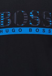 T-shirt in cotone nero con grande testo "BOSS" in strisce blu e blu navy, con una fascia blu solida che mostra "HUGO BOSS" sotto.