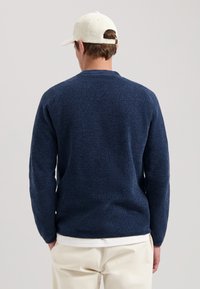 Granatowy sweter dzianinowy o teksturowanym wzorze, okrągłym dekolcie i długich rękawach. Połączony z jasnymi spodniami dla kontrastu.