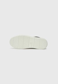 Zwarte sneakerzool met een gestructureerde witte rubberen basis, voorzien van een rechthoekig logo en ondiepe groeven voor grip.