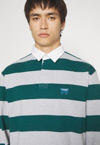 Groene en grijze gestreepte langemouwen polo shirt met een witte kraag en een Wrangler logo patch op de borst, voorzien van een knopenlijst.