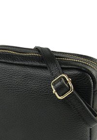 Zwarte leren tas met een gestructureerd oppervlak, een gouden rits en een verstelbare band met een rechthoekige metalen gesp.