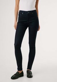 Tmavě modré skinny džíny vyrobené z denimu, s vysokým pasem, minimalistickým designem a nenápadnými předními kapsami, doplněné černými botami.