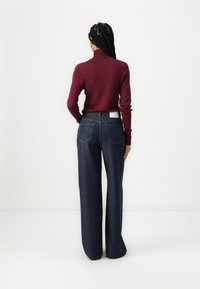 Suéter burdeos ajustado con cuello de tortuga combinado con jeans de mezclilla oscura de pierna ancha que cuentan con dos bolsillos traseros y una etiqueta de marca visible.