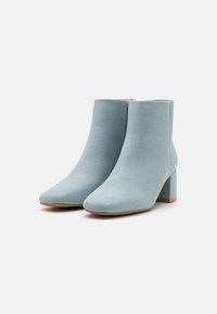 Bottines bleu clair en tissu texturé, avec un bout pointu et un talon carré imposant. Fermeture à glissière sur le côté.