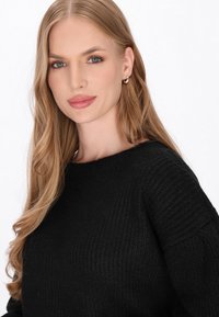 Pulover negru din tricot, cu un model texturat, decolteu larg și umeri lăsați, complementar cu păr lung și ondulat și cercei cu perfecție.