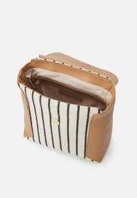 Brown leather handbag featuring a white and black striped fabric front, open top, and a zippered interior pocket. Gold button closure detail.