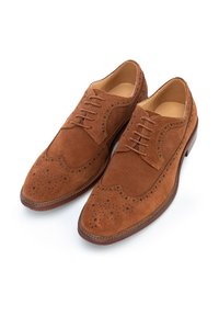 Mocasines de ante marrón con diseño de punta de ala, detalles perforados y cierre de cordones. Forro interior suave y suela de cuero resistente.
