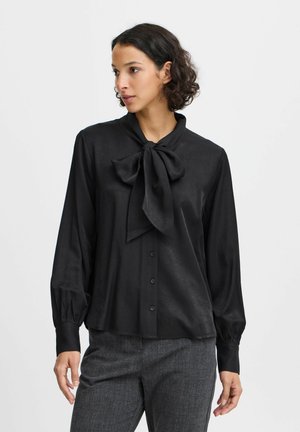 Schwarze Bluse mit einer Frontschleife, langen Ärmeln und Knopfleiste. Glatte Textur mit leichtem Glanz, mit gerafften Manschetten und lockerer Passform.