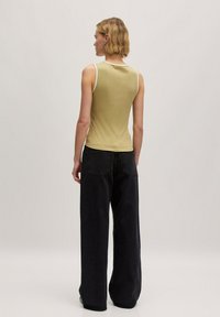 Groene tanktop met witte randen, aansluitend ontwerp; gecombineerd met wijde zwarte jeans; gladde textuur; eenvoudige achterkant.
