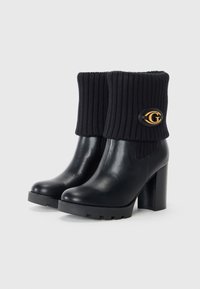 Black leather ankle boots with a ribbed knit upper. Chunky high heel and platform sole. Features a gold logo accent on the side.