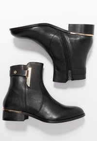 Bottes basses en cuir noir avec un bout arrondi, un petit talon carré et des détails dorés. Dotées d'une fermeture éclair latérale pour faciliter l'enfilage.