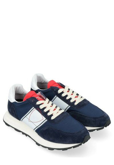 Baskets de sport bleu marine avec un dessus en daim et synthétique, accents blancs, col rouge, lacets crème et semelle en caoutchouc texturé.