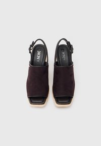 Μαύρα σανδάλια από σουέντ με ανοιχτά δάχτυλα, μπεζ υφή στην σόλα και λουράκι στο αστράγαλο. Το λογότυπο DKNY είναι ορατό στην εσωτερική σόλα.