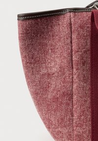 Piros szövet táska texturált mintával, sötétbarna bőr díszítéssel a felső részen, széles, nyitott kialakítással.