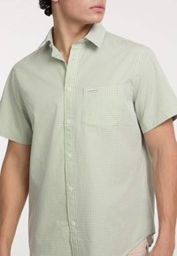 Camicia a maniche corte con bottoni in un motivo a quadretti verde chiaro, realizzata in cotone, con taschino sul petto e etichetta di marca sulla tasca.
