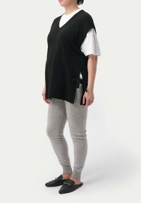 Svart stickad ärmlös tröja med V-ringning, bärs över en vit t-shirt; ihop med grå leggings och svarta slip-on skor. Sidobåge detalj.