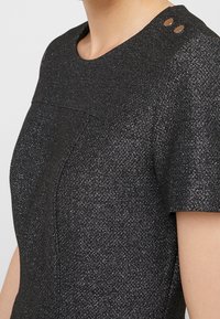 Czarna metaliczna sukienka o teksturowanym wykończeniu, z krótkimi rękawami, okrągłym dekoltem oraz dwoma okrągłymi ozdobami w okolicy ramienia.