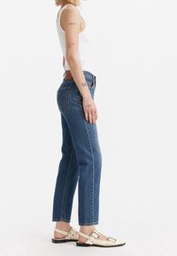 Blauwe denim spijkerbroek met hoge taille en rechte pijpen, met stikdetails, een leren achterkantlabel en gecombineerd met witte platte sandalen.