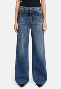 Weite Denim-Jeans in Mittelblau mit einer verblassten Waschung, verziert mit schwarzen Nieten auf der Vorderseite. Verfügt über ein klassisches Fünf-Taschen-Design.