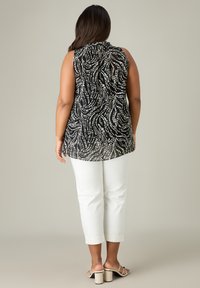 Svart ärmlös topp med ett vitt abstrakt mönster; matchat med vita cropped byxor och beige klacksandaler med blockklack. Slät textur.