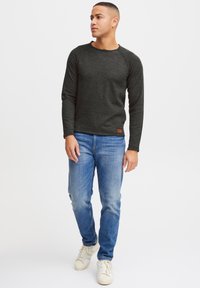 Donkergrijze longsleeve t-shirt met een ronde halslijn, raglanmouwen, gecombineerd met lichtblauwe jeans en witte sportschoenen.