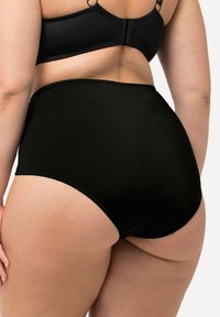 Zwarte hooggesneden onderbroek gemaakt van zachte stof, met een gegolfde rand en een ontwerp met volledige bedekking. Achteraanzicht getoond, geen patronen.