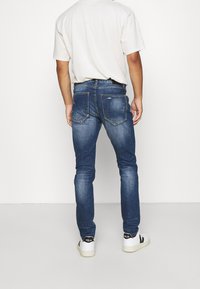 Modré džíny s úzkým střihem, které mají zadní kapsy s jemnými švy. Doplněno o bílé tenisky.