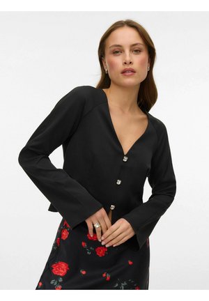 Must pikkade varrukatega top V-kujulise kaelusega, millel on dekoratiivsed nööbid ja sile tekstuur. Kandmise all lillemustriga seelik.