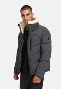 Grå puffjacka med fleece-fodrad krage, dragkedja fram och quiltad design. Har två sidofickor och en logga på bröstet.