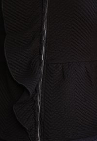 Svart kviltat tyg med diagonala sömmar och en silverfärgad dragkedja som löper vertikalt genom mitten.