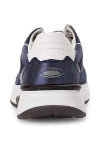 Marineblauwe en witte sportieve schoen, gemaakt van leer en mesh, met een textuur op de achterkant, een dikke zool en logodetails.
