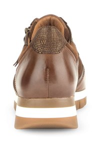 Bruine leren sneaker met een gestructureerde bruine achterkant, witte accentlijn op de zool en een gladde afwerking. Ritssluiting aan de zijkant.