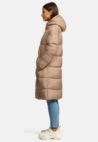 Beige puffer coat with a hood, featuring quilted sections, side pockets, and a logo accent on the sleeve. Paired with light blue jeans and sneakers.