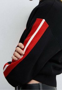 Mustat neulepaidat, joissa on punaiset raidat hihoissa ja ribbitekstuuri. Malli on istuva ja siinä on minimalistinen tyyli.